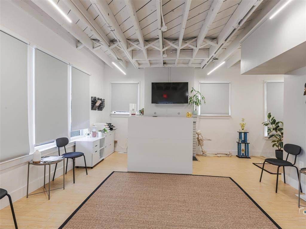 4310 Gaston Avenue, #103, Dallas, TX 75246 Exposed wood beam ceiling with linear lighting, light wood-finish flooring, multiple windows with roller shades, built-in reception desk, and a wall-mounted television