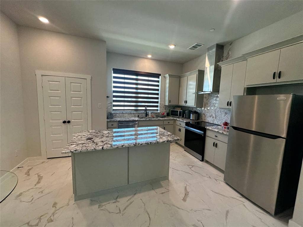 Modern kitchen featuring stainless steel appliances, white cabinetry with hardware accents, and a large waterfall-edge island with patterned quartz countertops