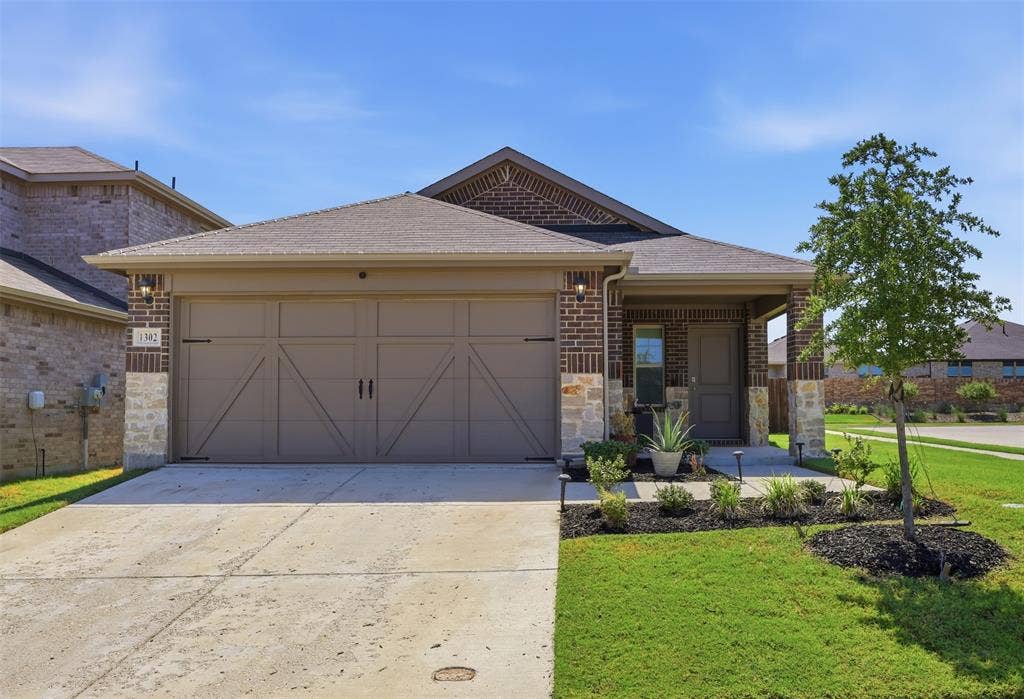 Brick and stone exterior with a covered porch, attached two-car garage, concrete driveway, and landscaped front yard
