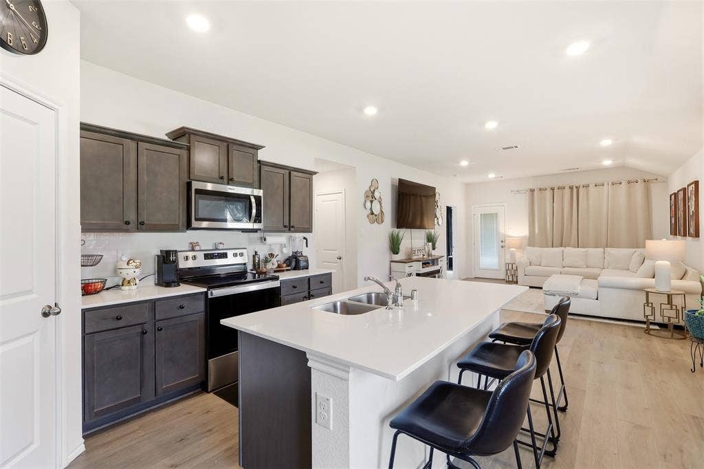 Open-concept living space featuring a kitchen island with seating, stainless steel appliances, dark wood-finish cabinetry, and wood-finish flooring