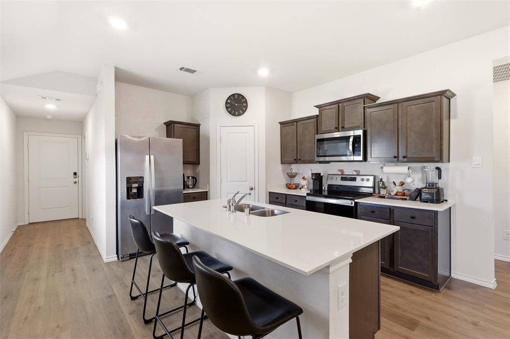 Kitchen featuring an island with a built-in sink, dark wood-finish cabinetry, stainless steel appliances, and wood-finish flooring