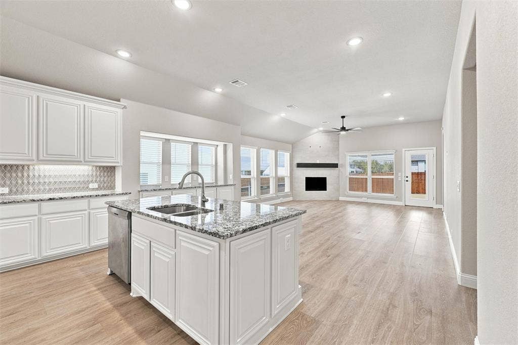 5225 Rowlan Row, Midlothian, TX 76065 Chef's kitchen featuring white cabinetry, a large center island with waterfall countertop and undermount sink, stainless steel appliances, and geometric tile backsplash