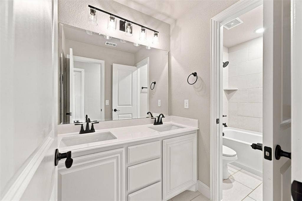 5225 Rowlan Row, Midlothian, TX 76065 Dual vanity with integrated sinks, white cabinetry, matte black fixtures, and a combined shower/tub with white subway tile surround