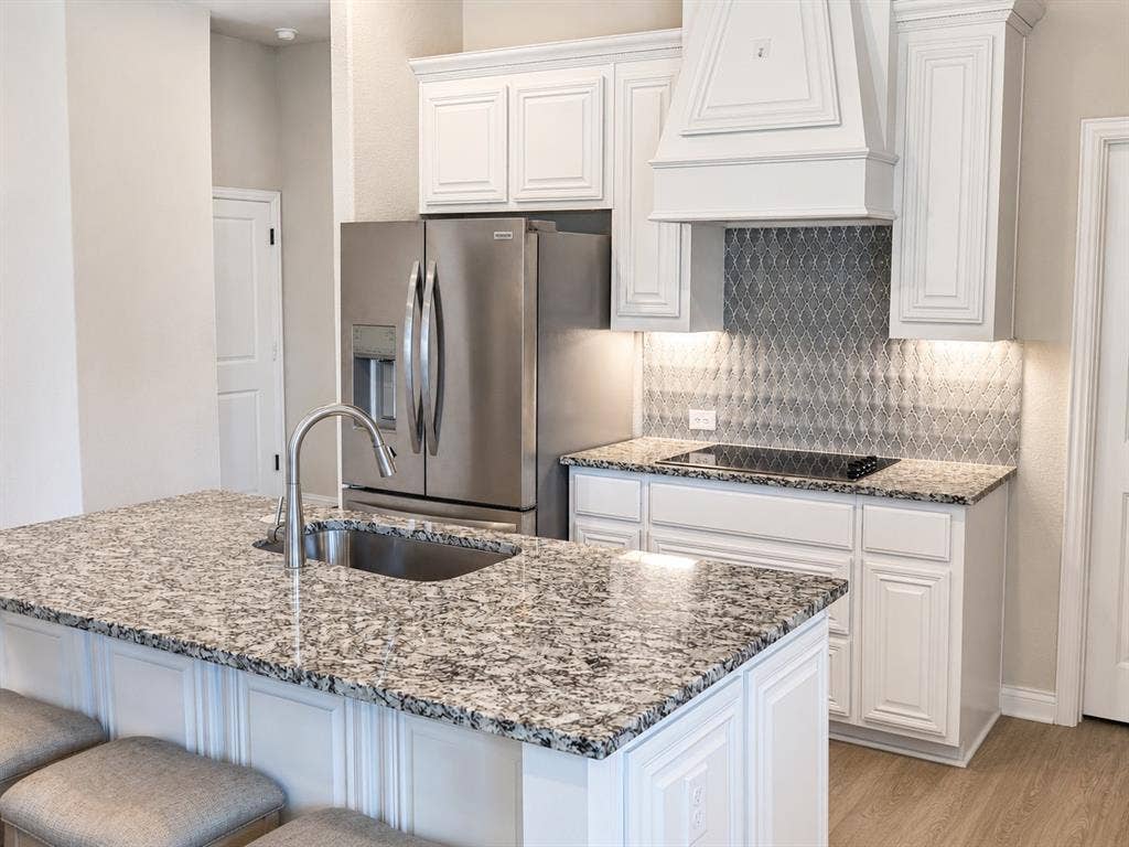 5225 Rowlan Row, Midlothian, TX 76065 Kitchen featuring a granite island with an undermount sink and gooseneck faucet, white cabinetry, stainless steel appliances, and a mosaic tile backsplash