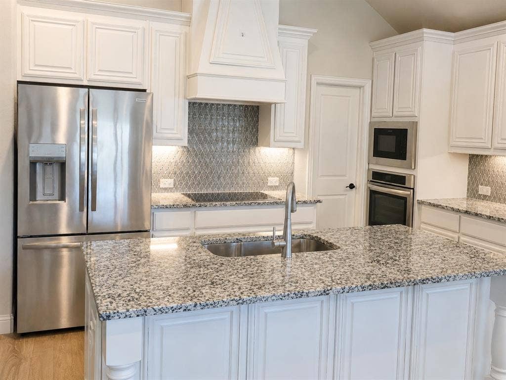 5225 Rowlan Row, Midlothian, TX 76065 White cabinetry, stainless steel appliances, speckled countertops, kitchen island with sink, and a decorative tile backsplash