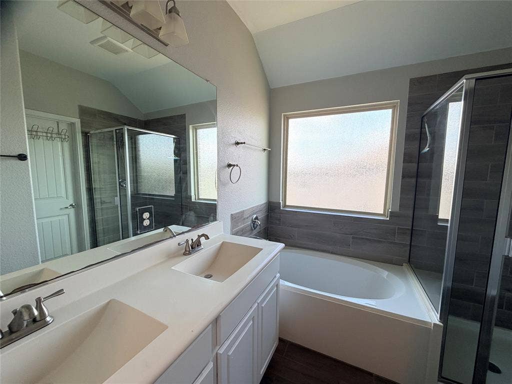 4103 Portrush Drive, Heartland, TX 75126 Double vanity with integrated sinks, full-width mirror, glass-enclosed shower, bathtub, and wood-finish flooring