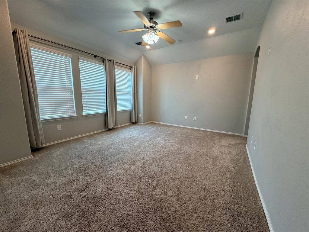 4103 Portrush Drive, Heartland, TX 75126 Spacious room featuring neutral carpet, multiple windows with blinds, a ceiling fan with integrated lighting, recessed lighting, and an arched doorway