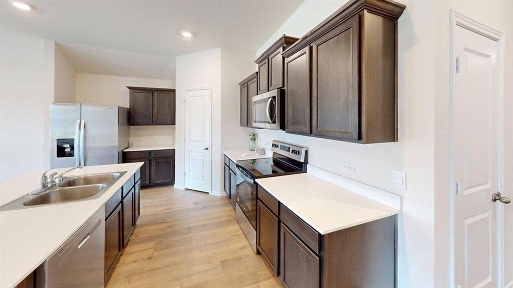 6534 Whitecap Drive, Princeton, TX 75407 Modern galley kitchen featuring stainless steel appliances, white quartz countertops, dark cabinetry with ample storage, wood-finish flooring, and an island with additional counter space