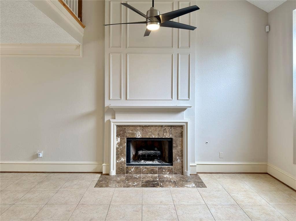 418 Newberry Street, Grand Prairie, TX 75052 Two-story living area featuring a fireplace with stone tile surround, decorative mantel, and paneling, complemented by a ceiling fan and light-toned tile flooring