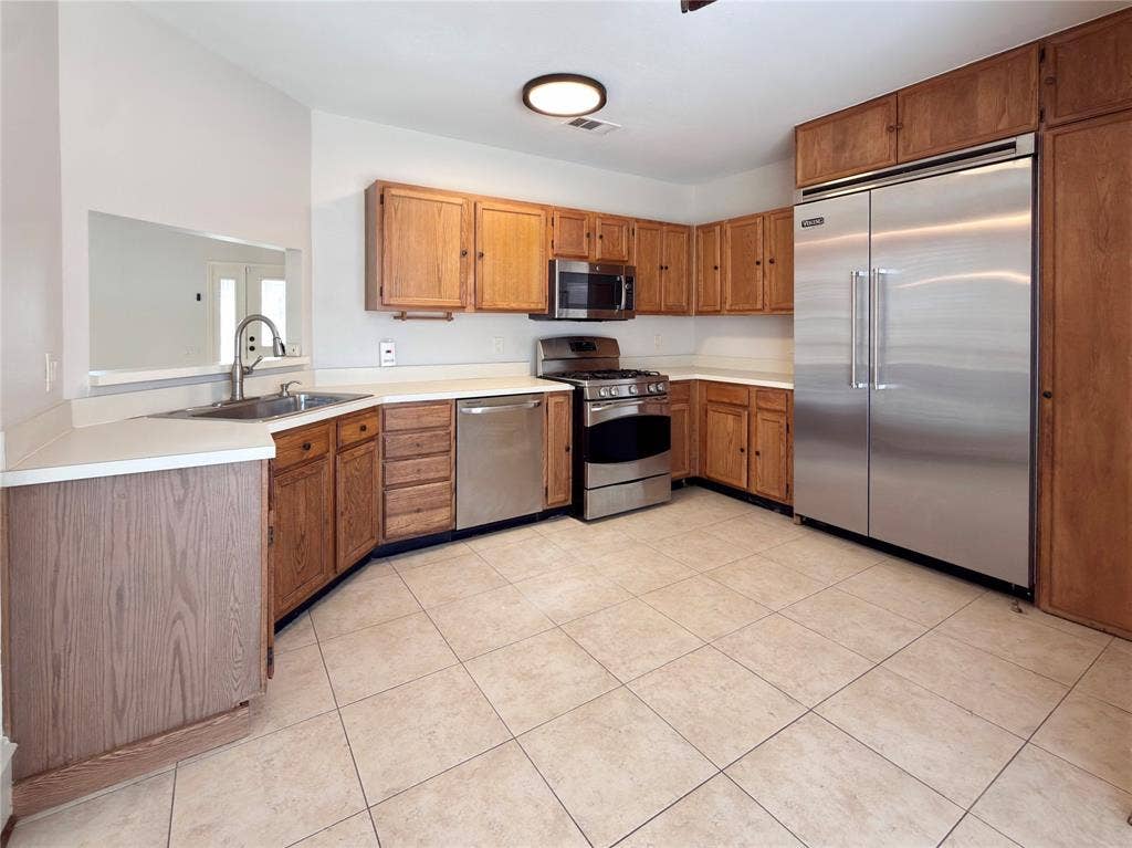 418 Newberry Street, Grand Prairie, TX 75052 Kitchen featuring wood cabinetry, stainless steel appliances, a stainless steel sink with a gooseneck faucet, light-colored countertops, and tiled flooring