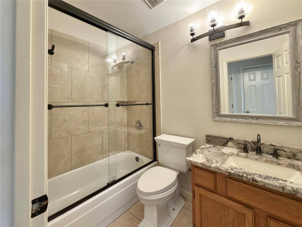 418 Newberry Street, Grand Prairie, TX 75052 Spa-inspired ensuite bathroom featuring a frameless glass-enclosed shower with tile surround, soaking tub, dual-sink vanity with granite countertop, wood cabinetry, and brushed nickel fixtures