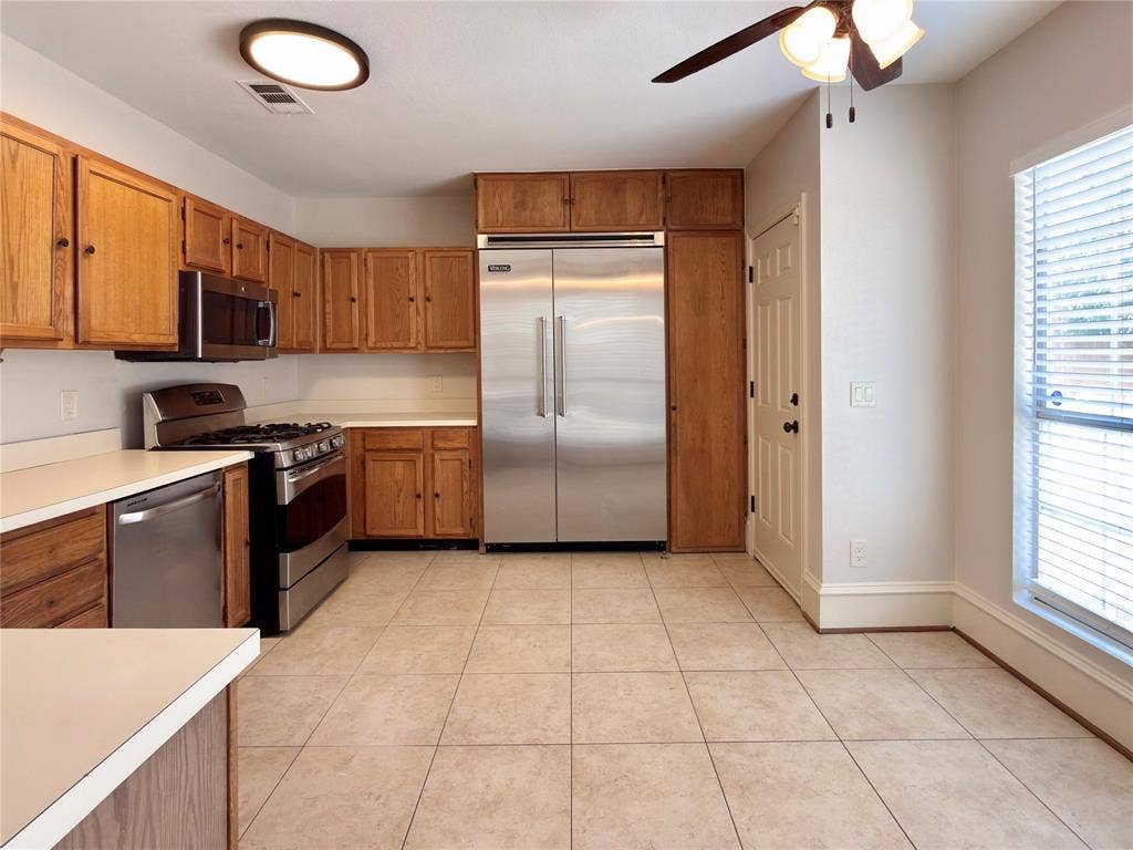 418 Newberry Street, Grand Prairie, TX 75052 Kitchen featuring stainless steel appliances, wood cabinetry, light-toned countertops, tile flooring, and a ceiling fan