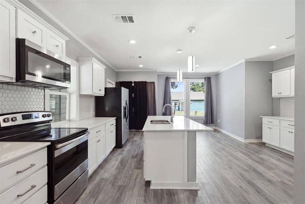 1812 Oneal Street, Greenville, TX 75401 Modern kitchen featuring white cabinetry, stainless steel appliances, a center island with sink, hexagonal tile backsplash, and wood-finish flooring