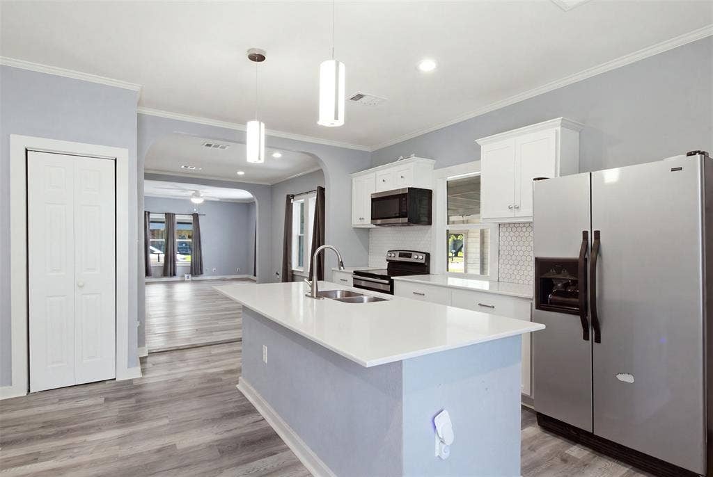 1812 Oneal Street, Greenville, TX 75401 Kitchen featuring an island with a light-toned countertop, stainless steel appliances, white cabinetry, and a hexagonal tile backsplash