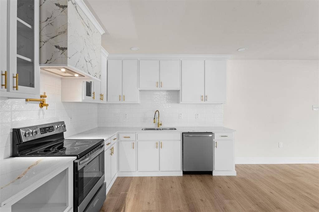 212 E Marguerita Drive, Garland, TX 75040 White cabinetry with gold-tone hardware, white subway tile backsplash, stainless steel appliances, and wood-finish flooring