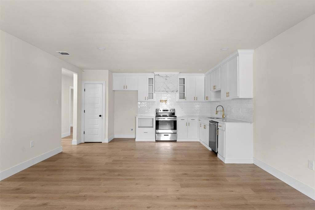 212 E Marguerita Drive, Garland, TX 75040 Open-concept kitchen featuring white cabinetry, stainless steel appliances, marble-patterned backsplash, gold-tone hardware, and wood-finish flooring