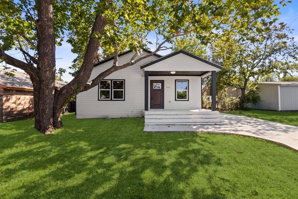 212 E Marguerita Drive, Garland, TX 75040 White siding exterior with black trim, covered porch, concrete driveway, and mature trees