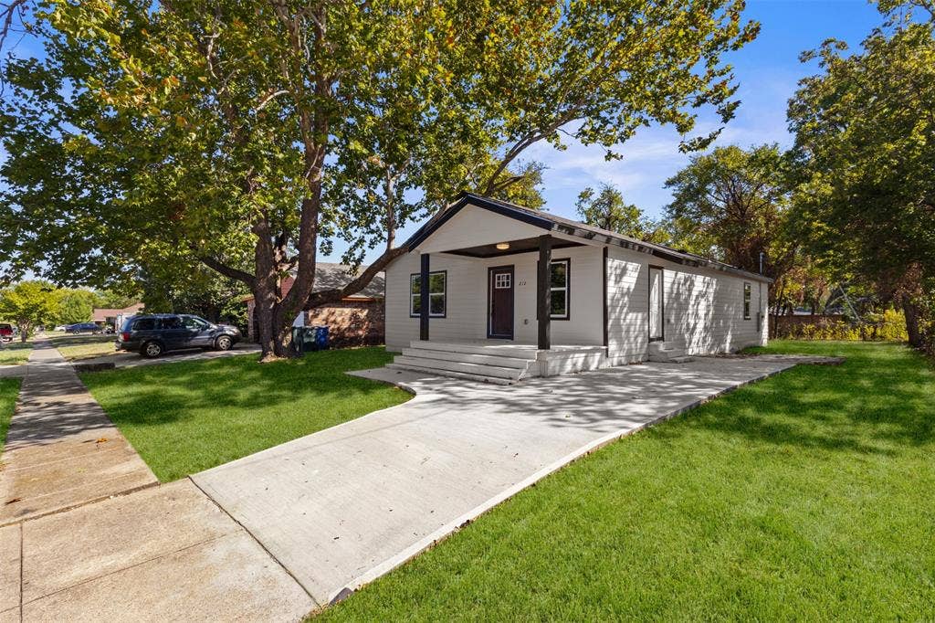 212 E Marguerita Drive, Garland, TX 75040 White siding exterior with dark trim accents, covered front porch, concrete driveway, and a mature tree