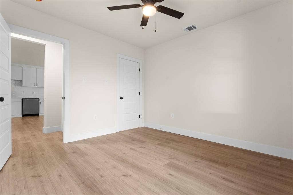 212 E Marguerita Drive, Garland, TX 75040 Wood-finish flooring, ceiling fan, white interior doors with black hardware, white walls, and a recessed doorway