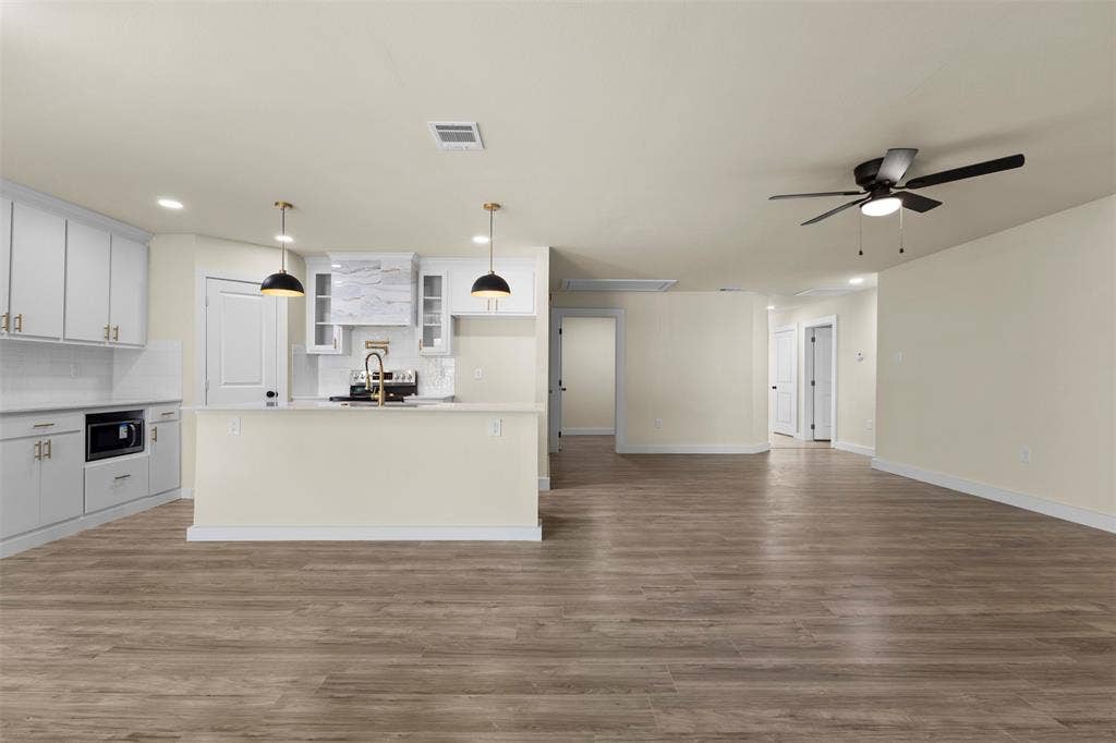 Kitchen featuring white shaker-style cabinetry, wood-finish flooring, a central island with a gold-toned faucet, pendant lighting, and a mounted ceiling fan