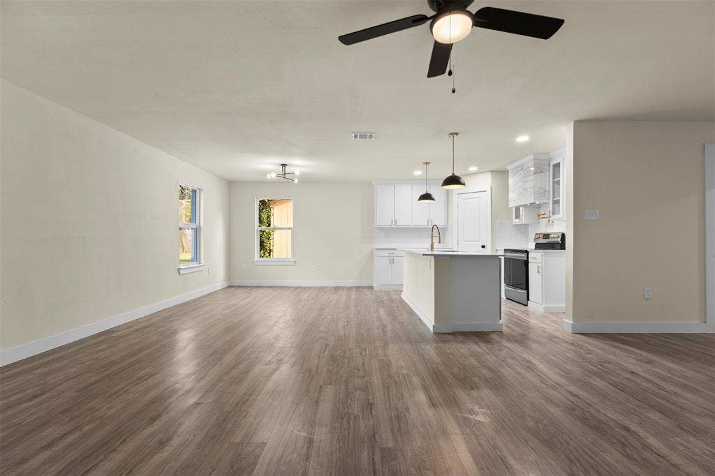 Open-concept area featuring wood-finish flooring, white cabinetry, a center island with pendant lighting, and recessed ceiling lights