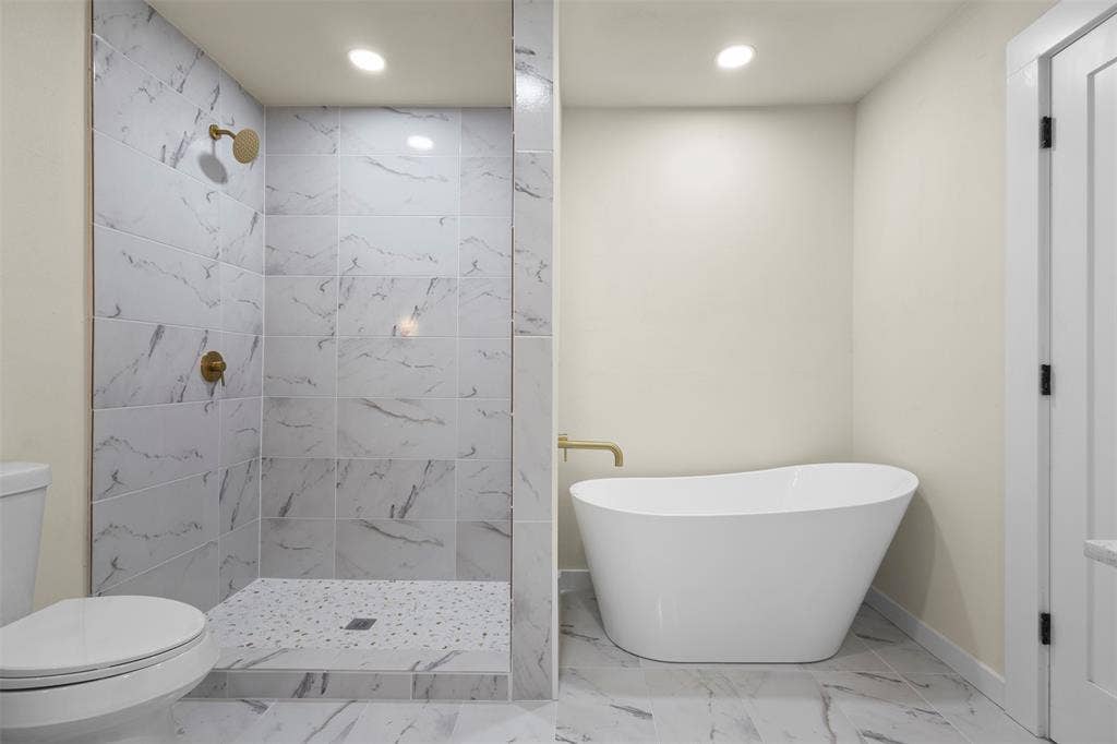 Walk-in shower with stone-finish tile surround and pebble-texture floor, freestanding soaking tub, metallic-finish hardware, and tile flooring