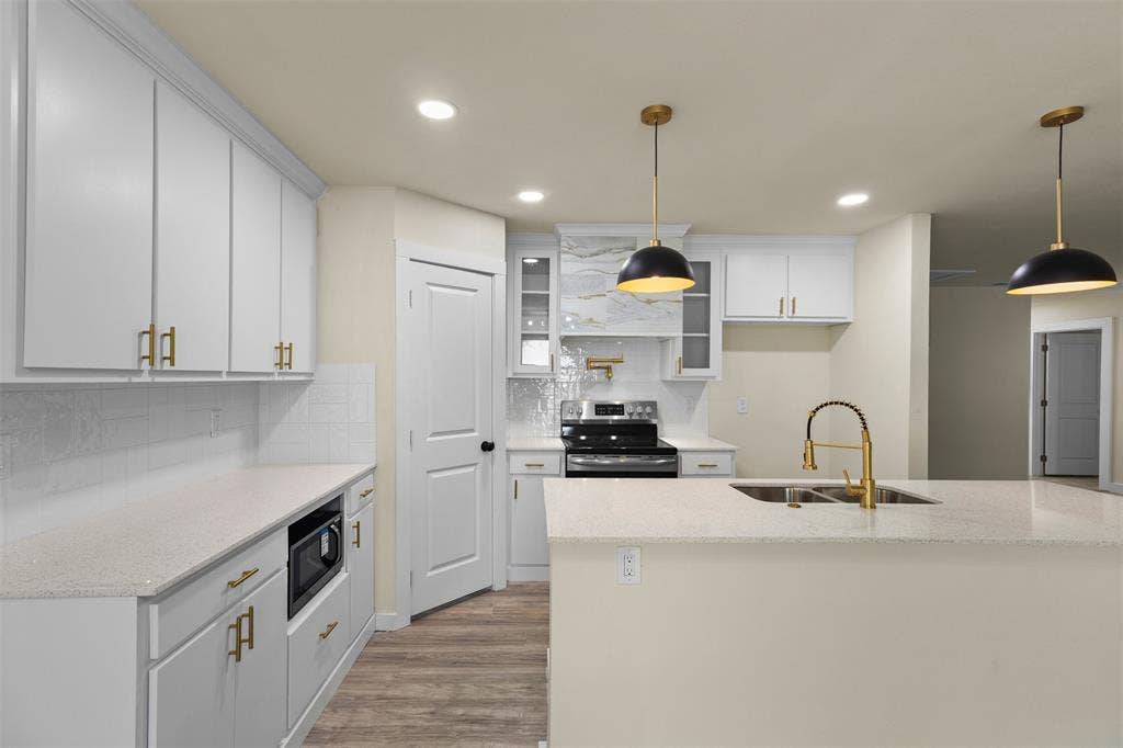 Kitchen featuring white shaker-style cabinetry with gold-tone hardware, quartz countertops, a central island with a gold-finish faucet, recessed lighting, and dual matte black pendant lights