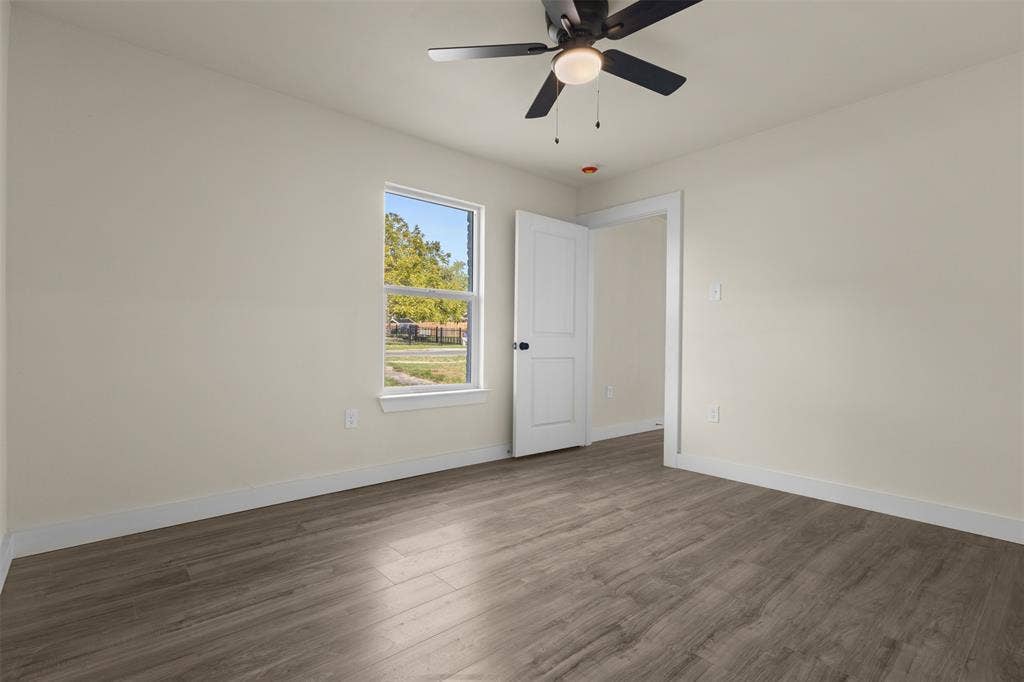 Room featuring wood-finish flooring, a multi-blade ceiling fan with integrated lighting, and a single-pane window with white trim