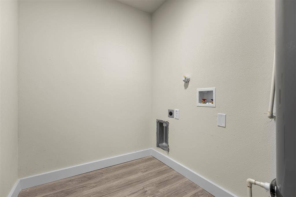 Dedicated space featuring wood-finish flooring, wall-mounted utility connections, and integrated plumbing access panels
