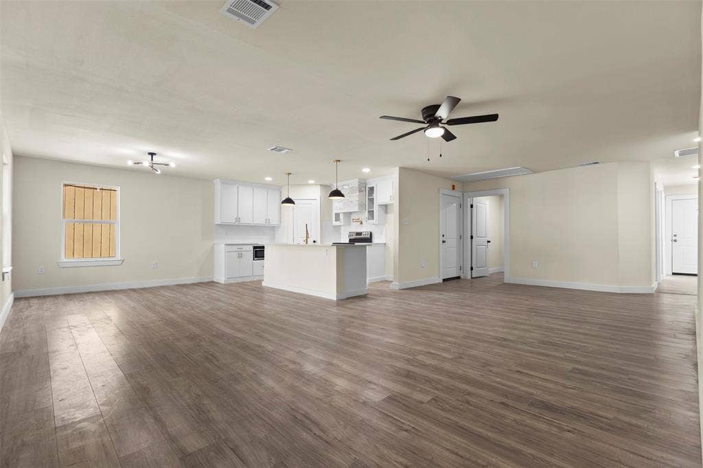 Open-concept interior featuring wood-finish flooring, white cabinetry, a center island with a stone-finish countertop, pendant lighting, and ceiling fans