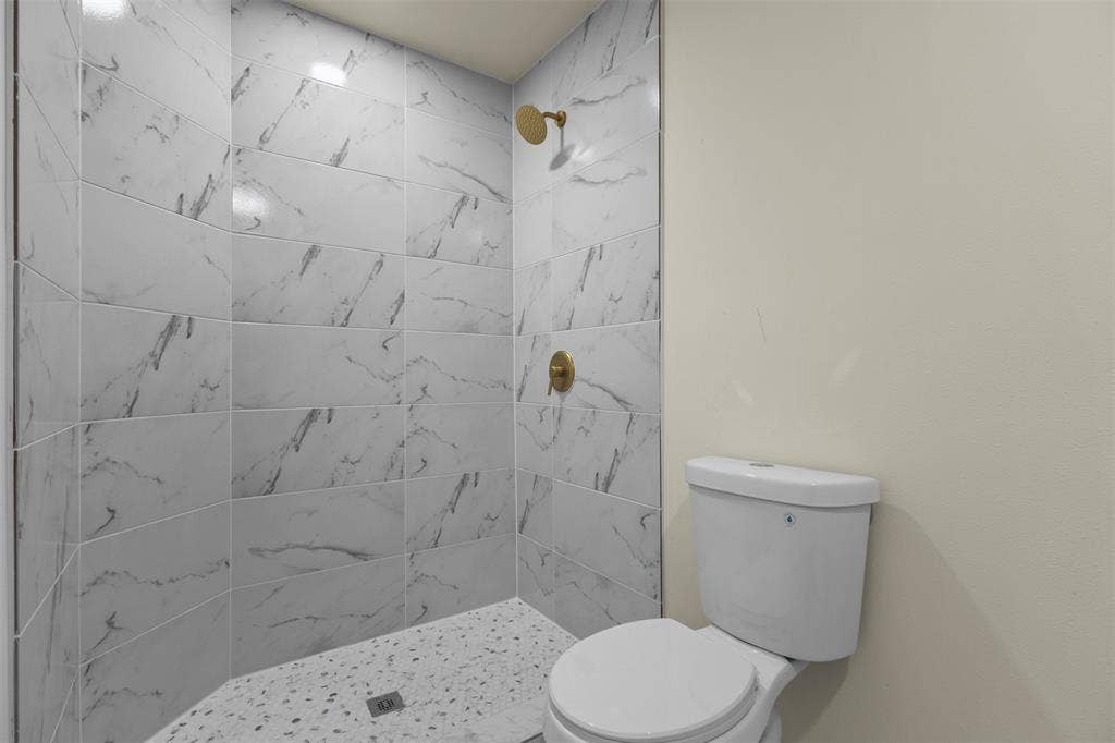 Shower stall with patterned tile wall surround, brass-finish fixtures, and a textured stone-finish shower pan