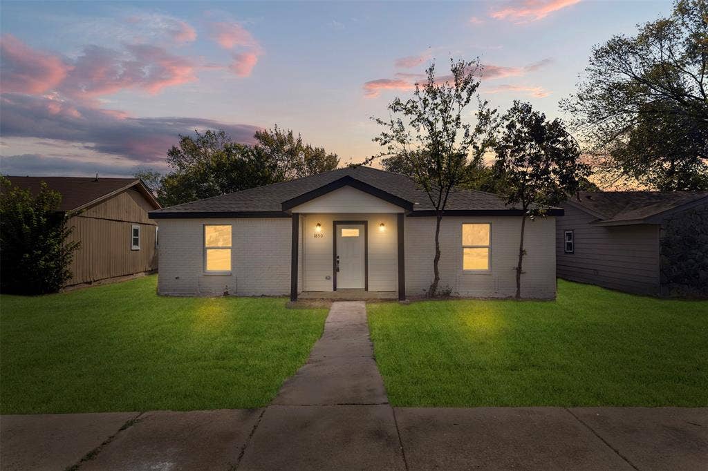 Single-story residence with painted brick exterior, covered front porch, dual wall-mounted light fixtures, and concrete walkway