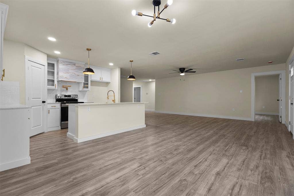 Open-concept interior featuring wood-finish flooring, white shaker-style cabinetry, a central island with a gold-tone faucet, and modern multi-arm pendant lighting