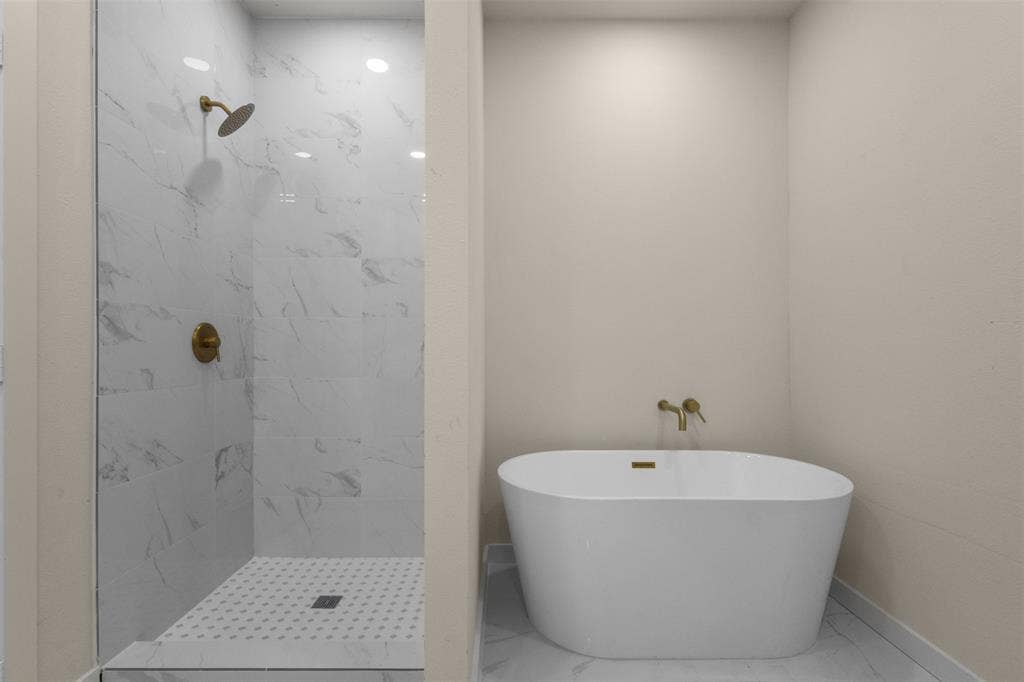 333 Levant Avenue, Dallas, TX 75217 Freestanding soaking tub, walk-in shower with glass enclosure, white marble-look tile walls, and gold-finish fixtures