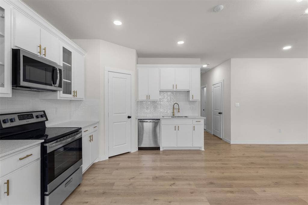 333 Levant Avenue, Dallas, TX 75217 Kitchen featuring white cabinetry with gold-finish hardware, stainless steel appliances, white subway tile backsplash, and light wood-finish flooring
