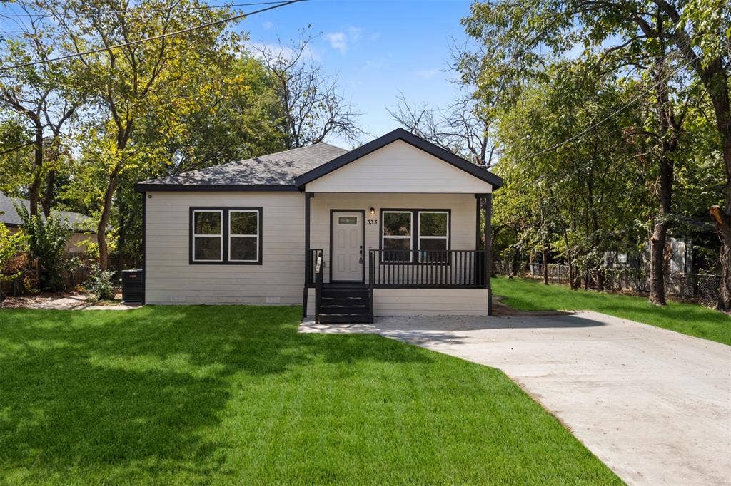 333 Levant Avenue, Dallas, TX 75217 Light-toned siding exterior with dark trim accents, covered front porch, dark-railed steps, asphalt shingle roof, and a concrete driveway
