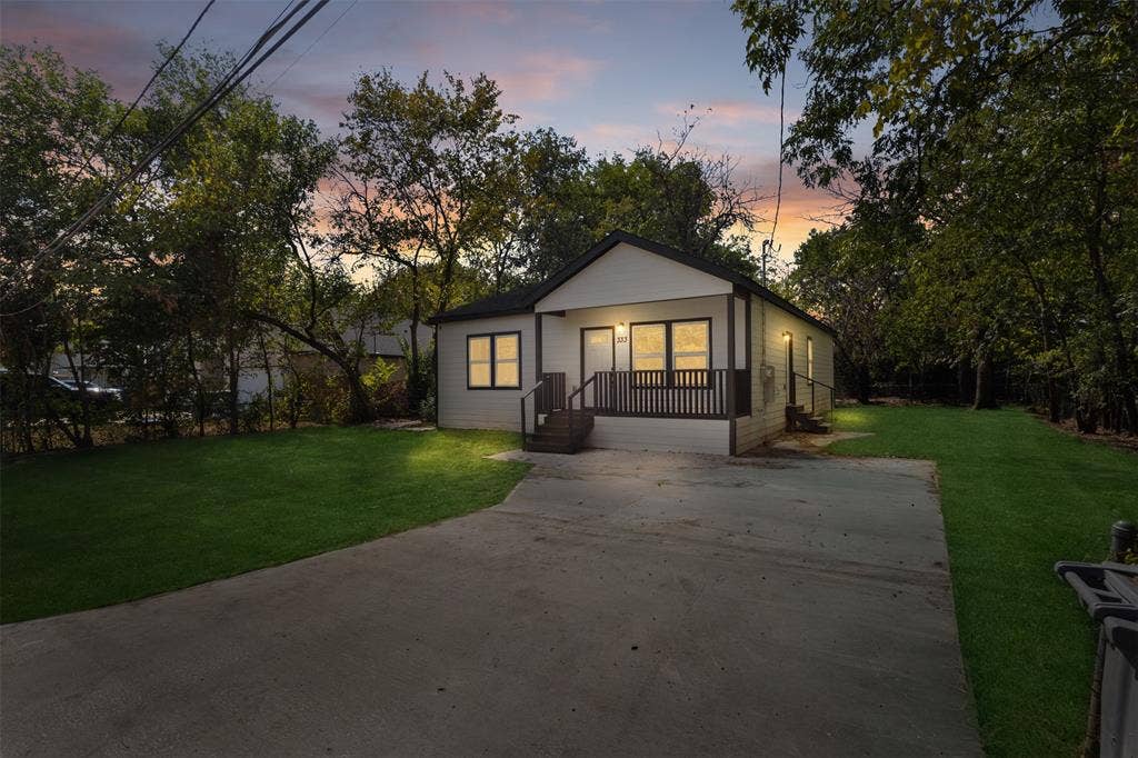 333 Levant Avenue, Dallas, TX 75217 White exterior siding with dark trim, covered front porch, concrete driveway, manicured lawn, and mature trees
