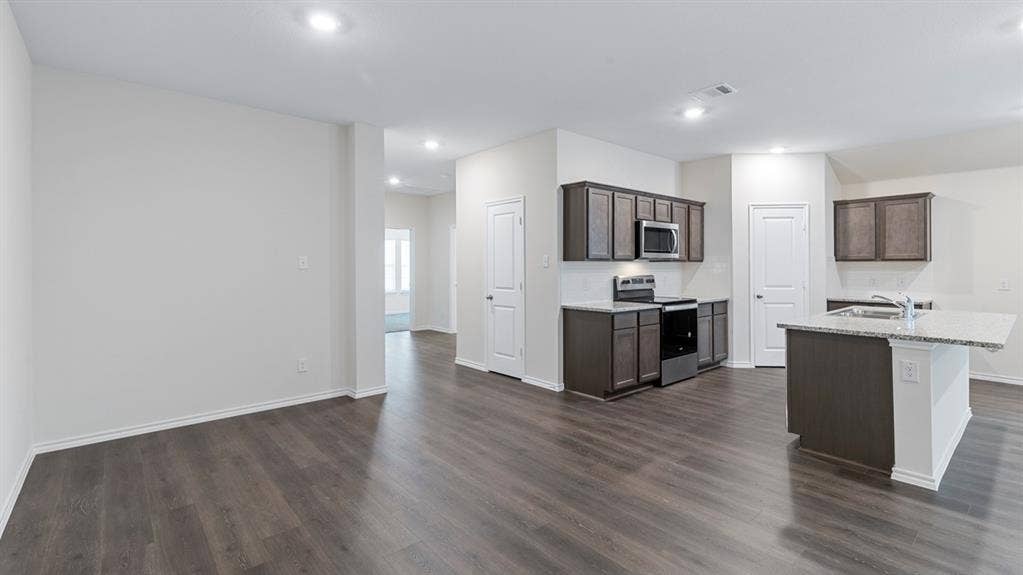 205 Brooks Street, Bullard, TX 75757 Open-concept kitchen with dark wood-finish cabinetry, stainless steel appliances, and an island featuring a light-toned countertop