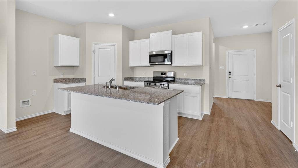 201 Brooks Street, Bullard, TX 75757 Kitchen featuring a central island, stainless steel appliances, granite countertops, white cabinetry, and wood-finish flooring