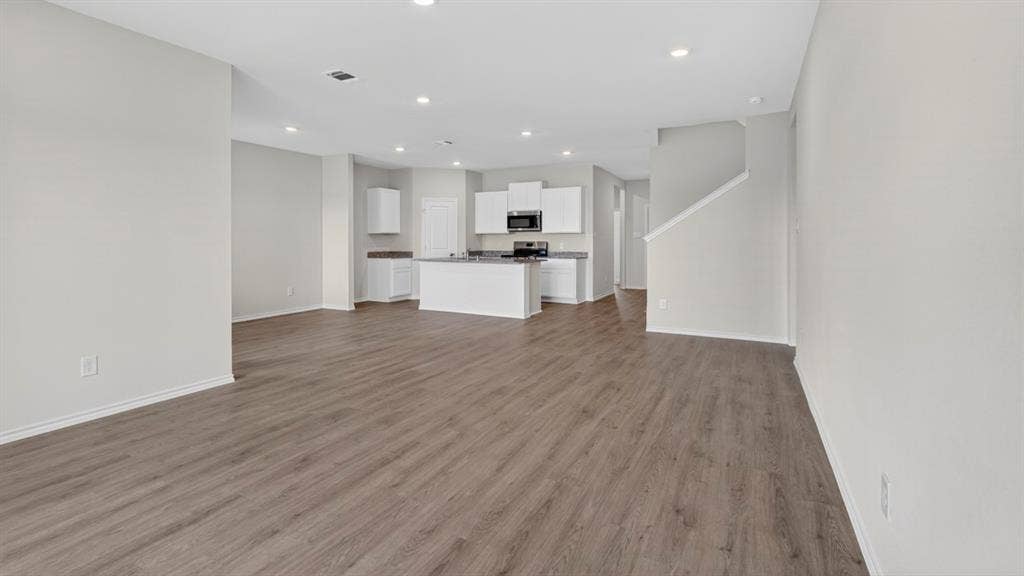 201 Brooks Street, Bullard, TX 75757 Expansive open-concept living area featuring wood-finish flooring, recessed lighting, a kitchen island with built-in cabinetry, and a staircase