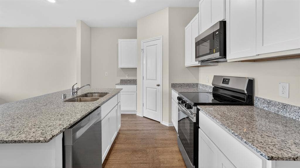 201 Brooks Street, Bullard, TX 75757 Kitchen featuring wood-finish flooring, white cabinetry, granite countertops, and stainless steel appliances including a range and microwave