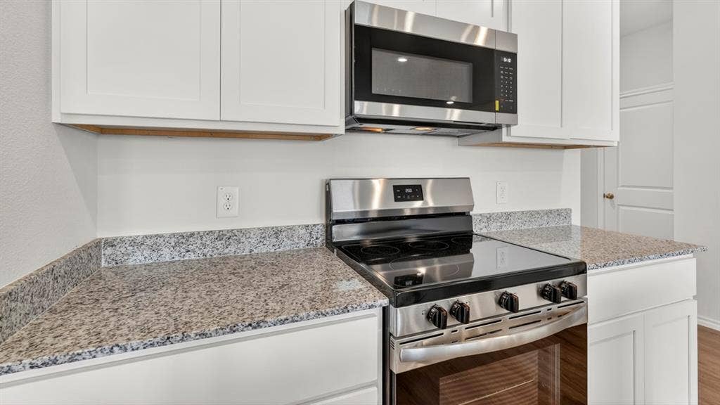 201 Brooks Street, Bullard, TX 75757 Stainless steel range, stainless steel microwave, stone countertops, white shaker cabinetry, and wood-finish flooring