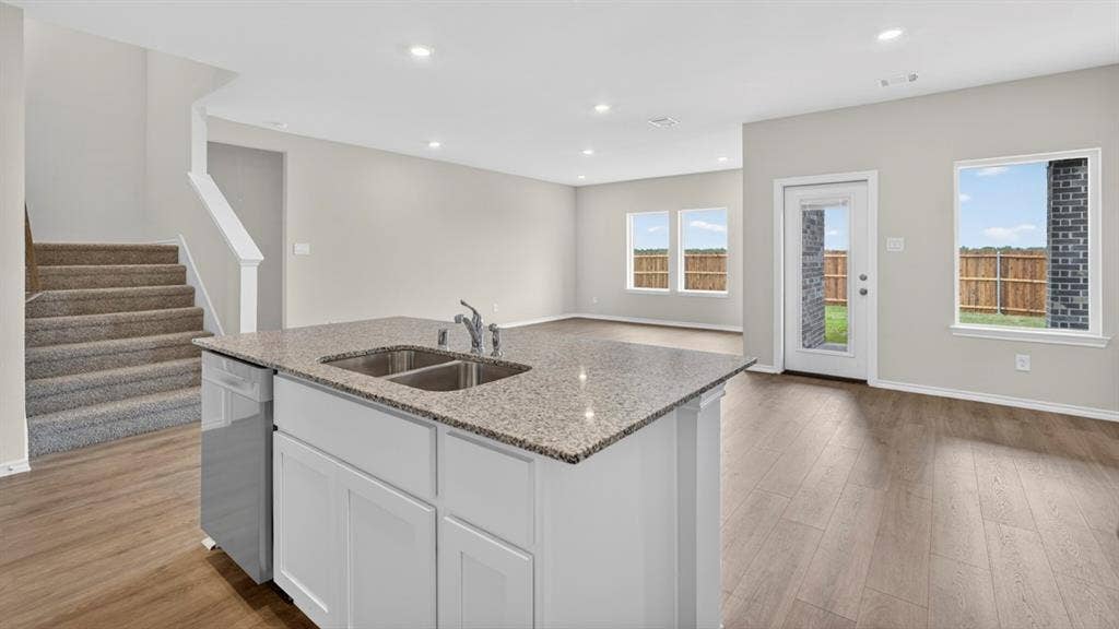 201 Brooks Street, Bullard, TX 75757 Kitchen island with granite countertop and stainless steel double sink, white shaker-style cabinetry, wood-finish flooring, recessed lighting, and multiple windows