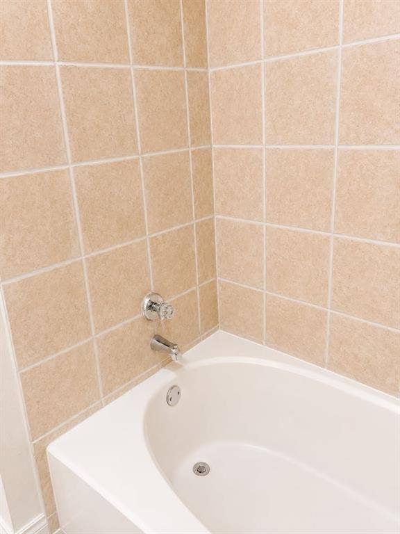4952 Berridge Lane, Dallas, TX 75227 White bathtub with a chrome faucet and clear acrylic handles, surrounded by square beige wall tiles