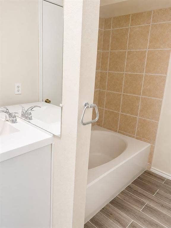 4952 Berridge Lane, Dallas, TX 75227 Bathtub with surrounding tile, wood-finish flooring, white vanity with integrated sink, and dual chrome faucets