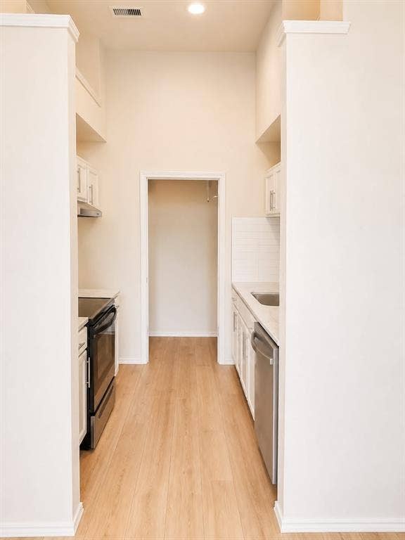 4952 Berridge Lane, Dallas, TX 75227 Galley kitchen with wood-finish flooring, white cabinetry, stainless steel appliances, and subway tile backsplash