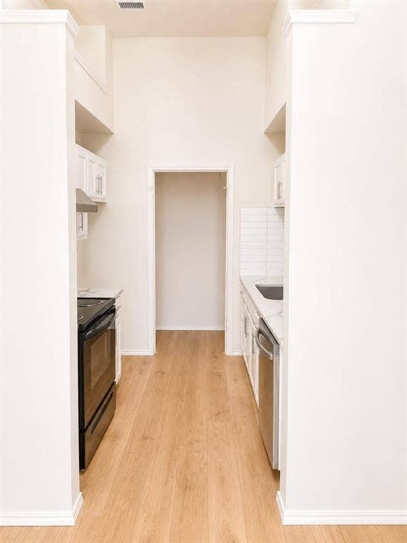 4952 Berridge Lane, Dallas, TX 75227 Galley kitchen featuring wood-finish flooring, white cabinetry, a black range, a stainless steel dishwasher, and a subway tile backsplash