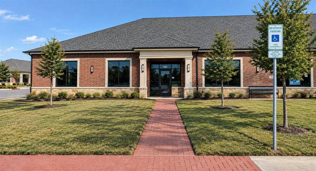 7700 Preston Rd, #1001, Frisco, TX 75035 Brick facade building featuring a dark shingle roof, stone foundation, and a red paver walkway