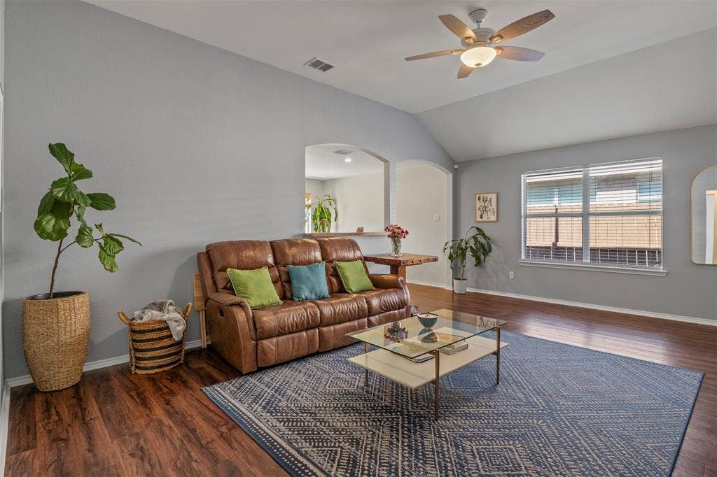 Vaulted ceiling with a ceiling fan, wood-finish flooring, and multiple windows