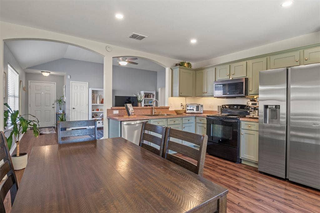 Kitchen featuring wood-finish flooring, recessed lighting, stainless steel refrigerator, black range, and sage-finish cabinetry
